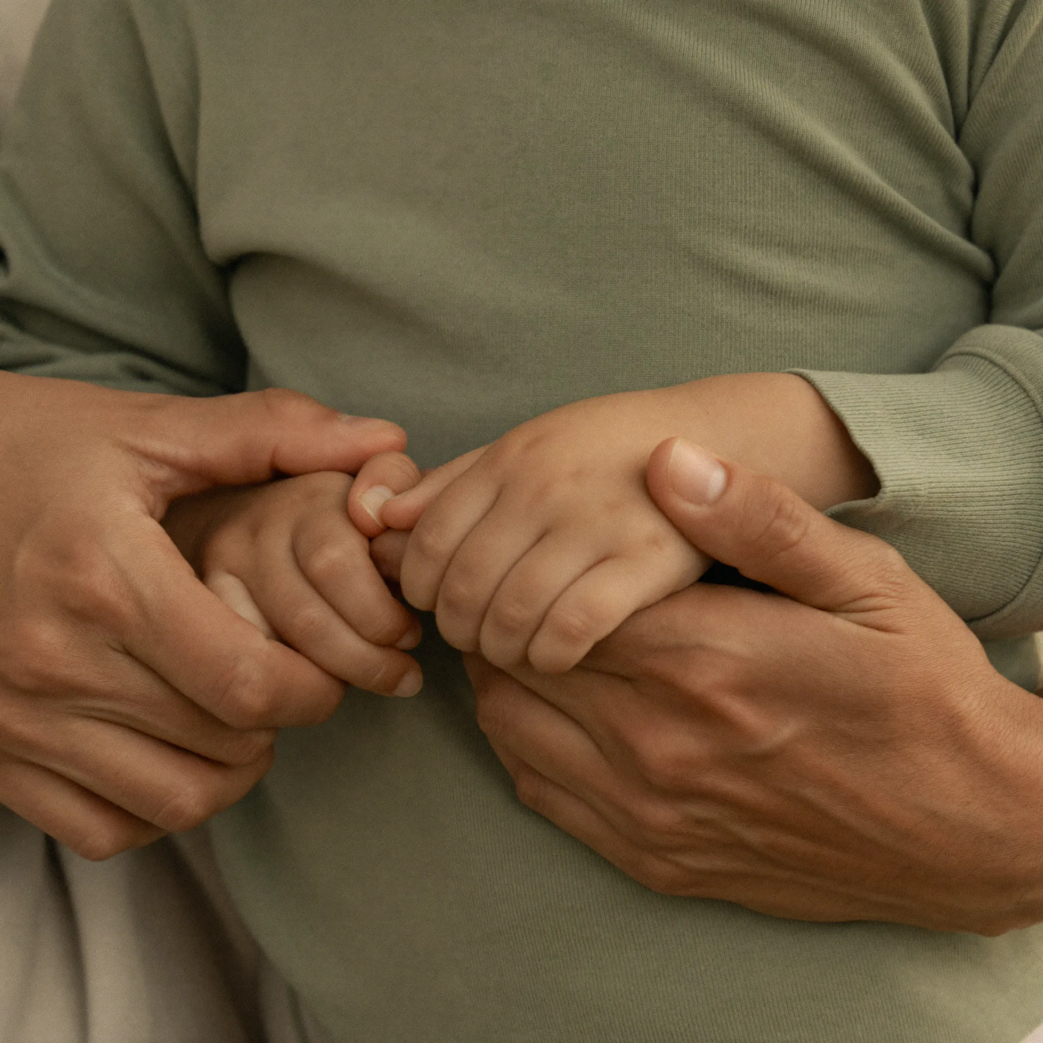 Gentle adult hands cradling a child's hands, representing compassionate family care